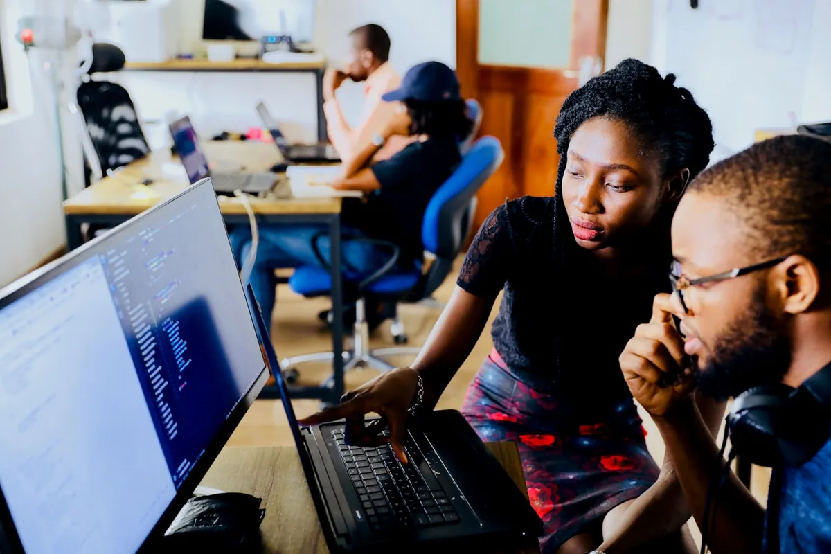 Two people reviewing code on a laptop during a website build, with the editor open on screen