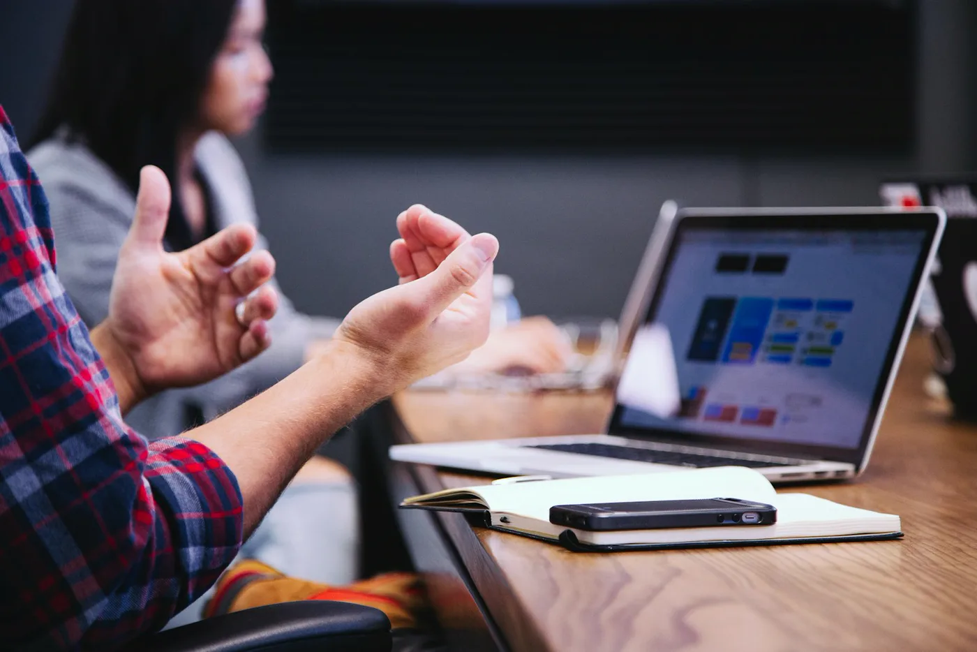 A working session in progress — someone explaining a plan across a table, with the plan open on a laptop
